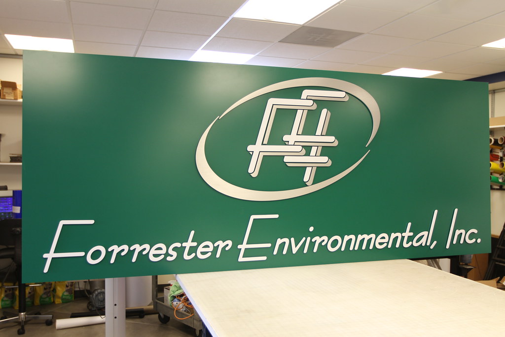 8' wide fabricated metal panel painted customer green with 3/8" thick cut aluminum lettering and logo assembled flush to face exterior use with cleat system for moutning