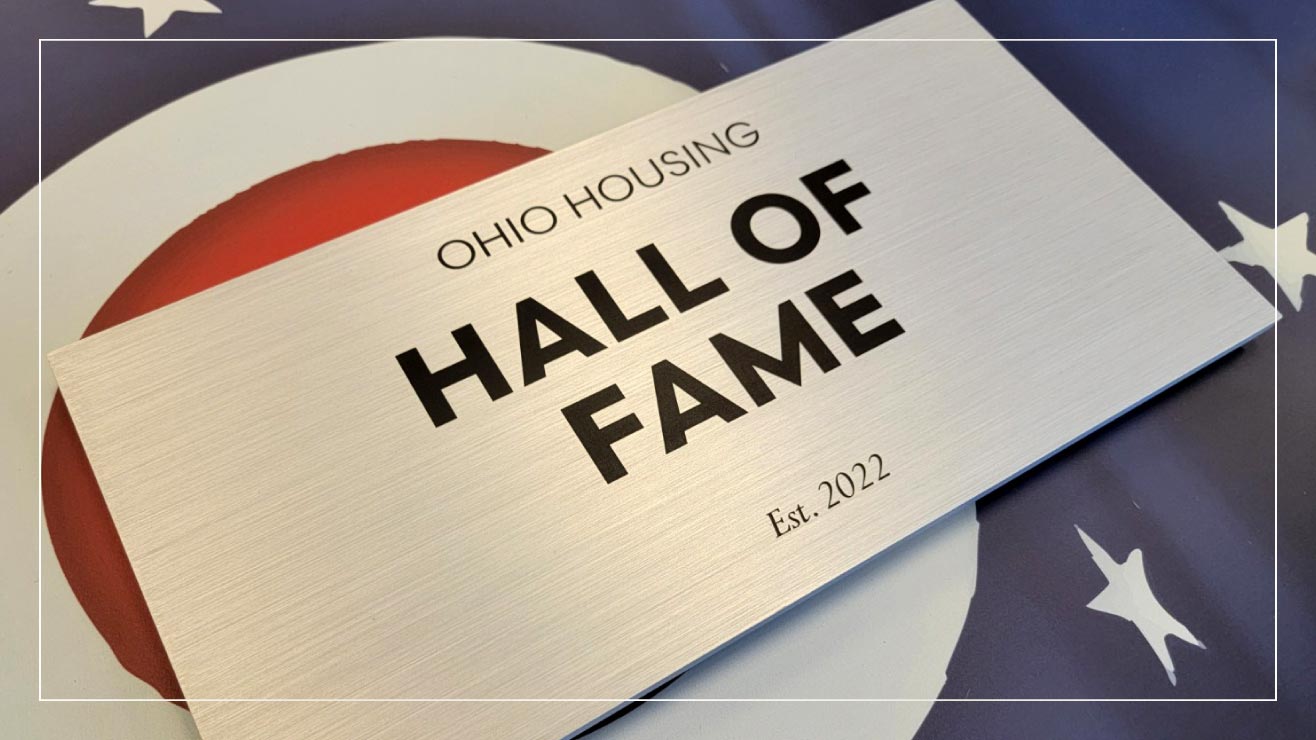 A stainless steel plaque is mounted on an acrylic sign to commemorate volunteers.