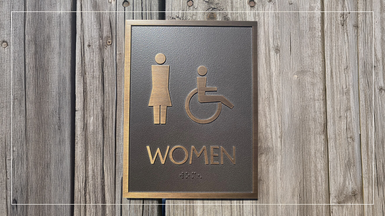 A bronze plaque with Braille lettering marks an accessible women's restroom.
