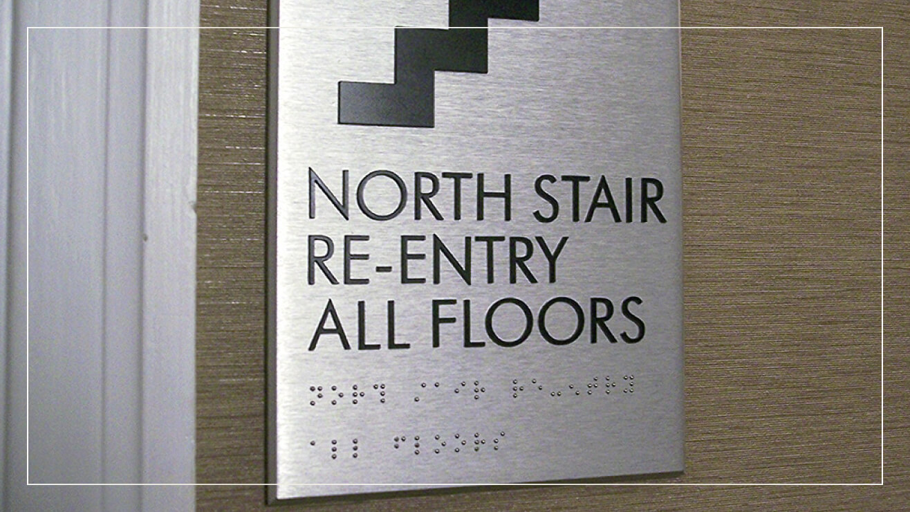 A stainless steel sign with braille marks stairs.